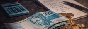 Imagem com dinheiro, cálculos e despesas do dia a dia, representando o controle financeiro, orçamento mensal e a realidade dos custos na vida do investidor.